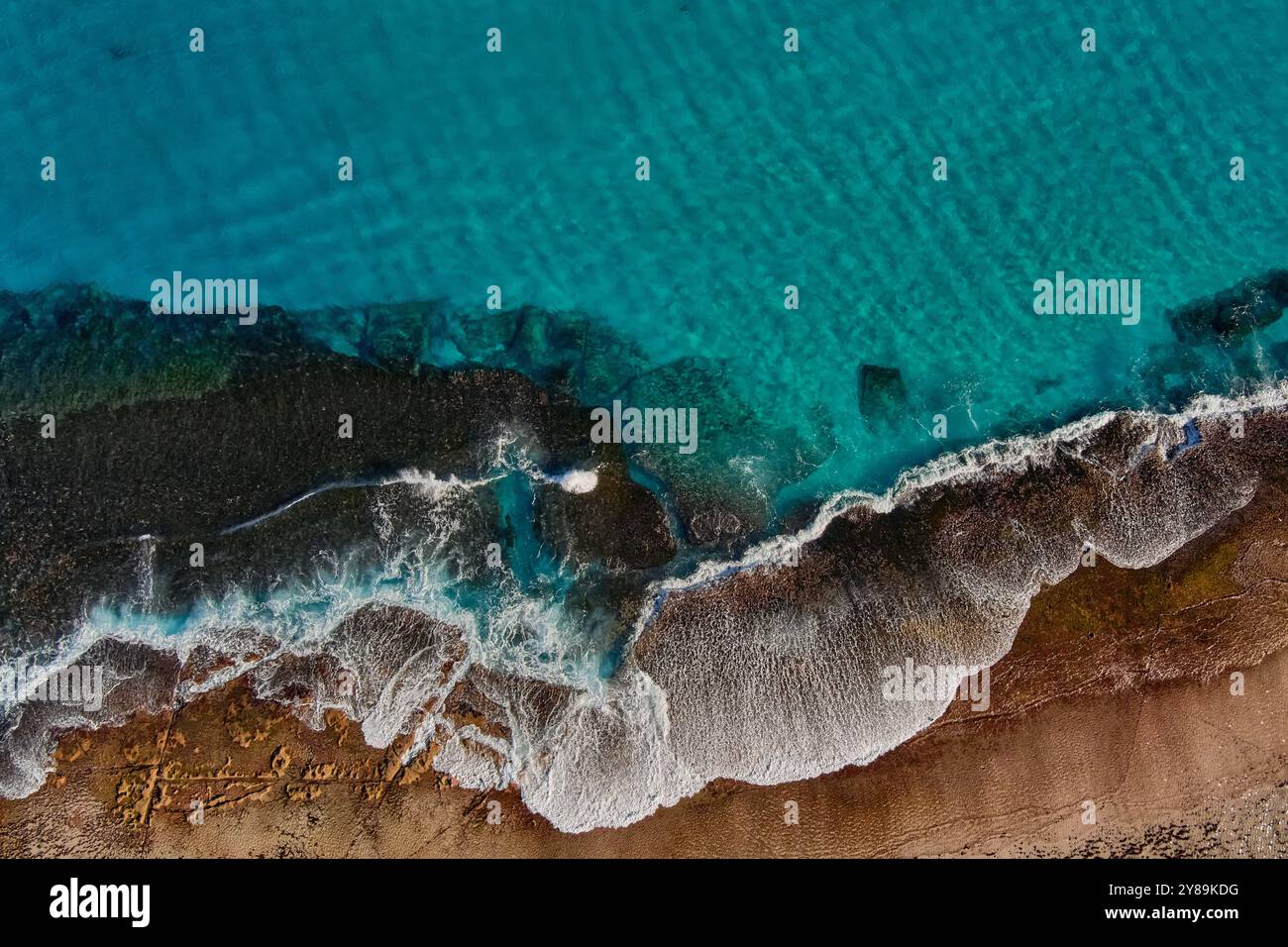waves break over a rocky outcrop in a clear white foam Stock Photo
