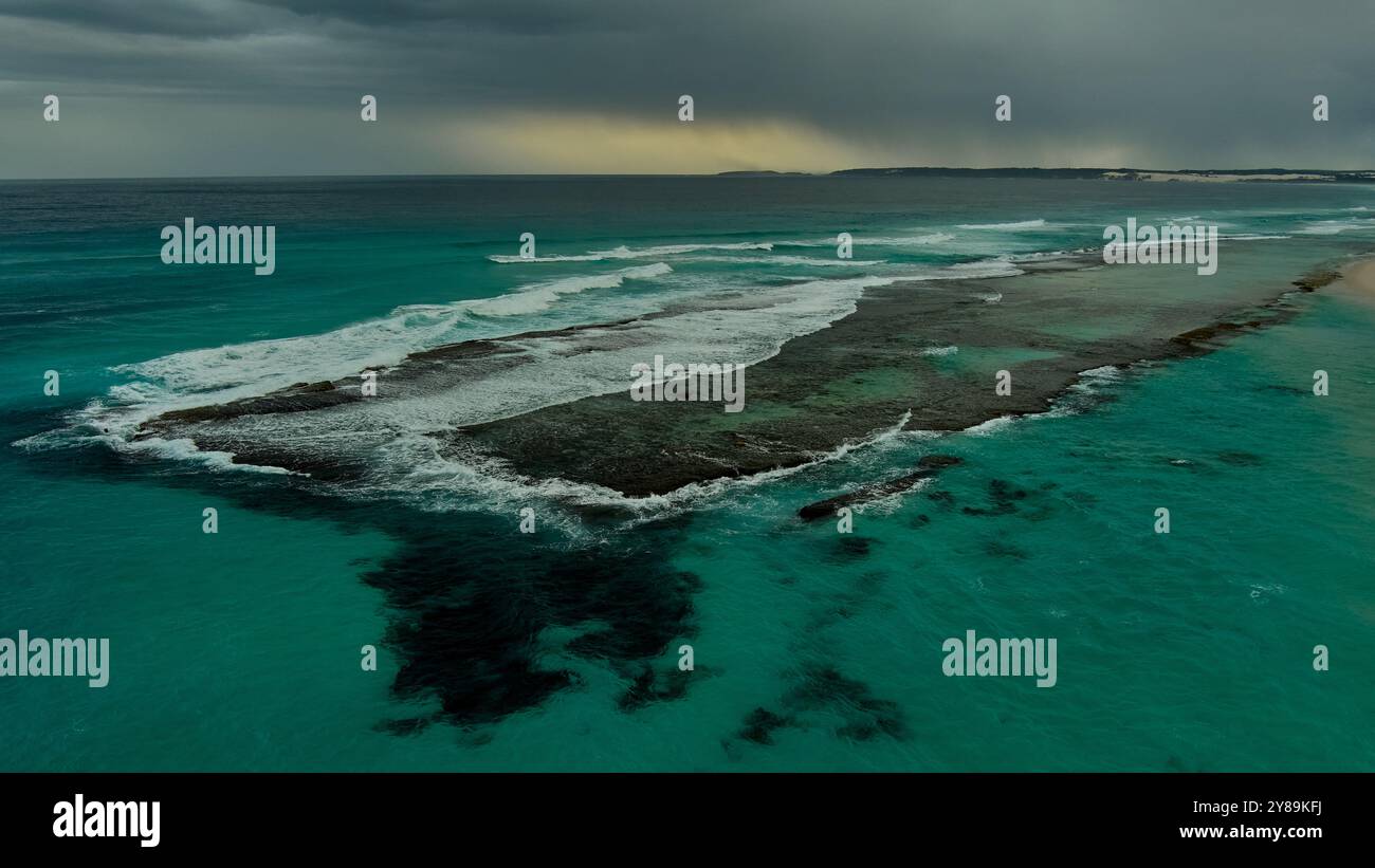 a storm approaches as waves break over a rocky reef Stock Photo