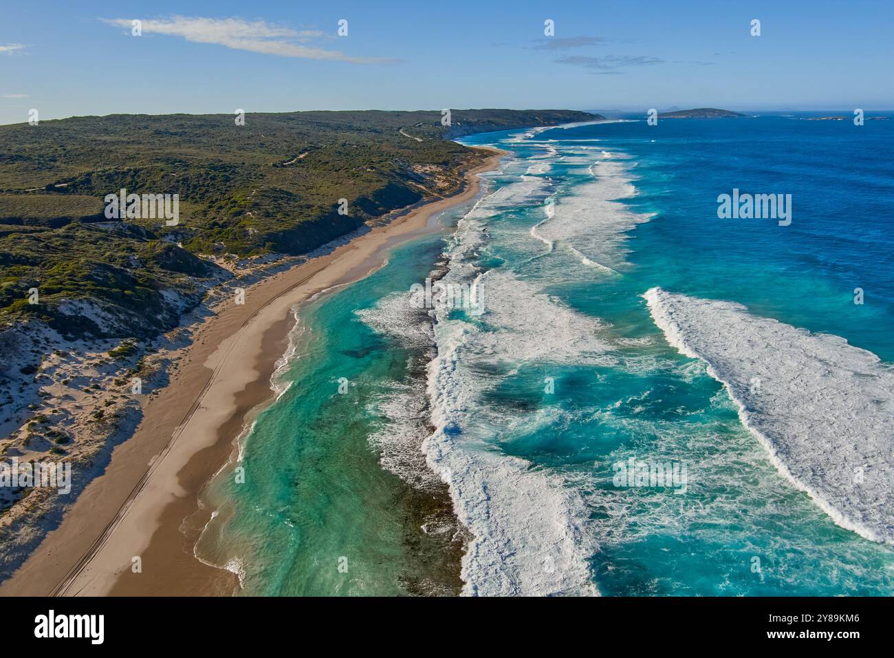 sand dunes line a beach with surf breaking over a rocky reef Stock Photo