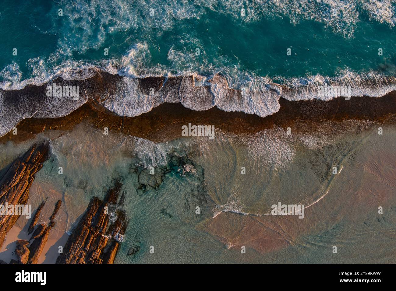 waves crash on shore as they meet a rocky reef Stock Photo