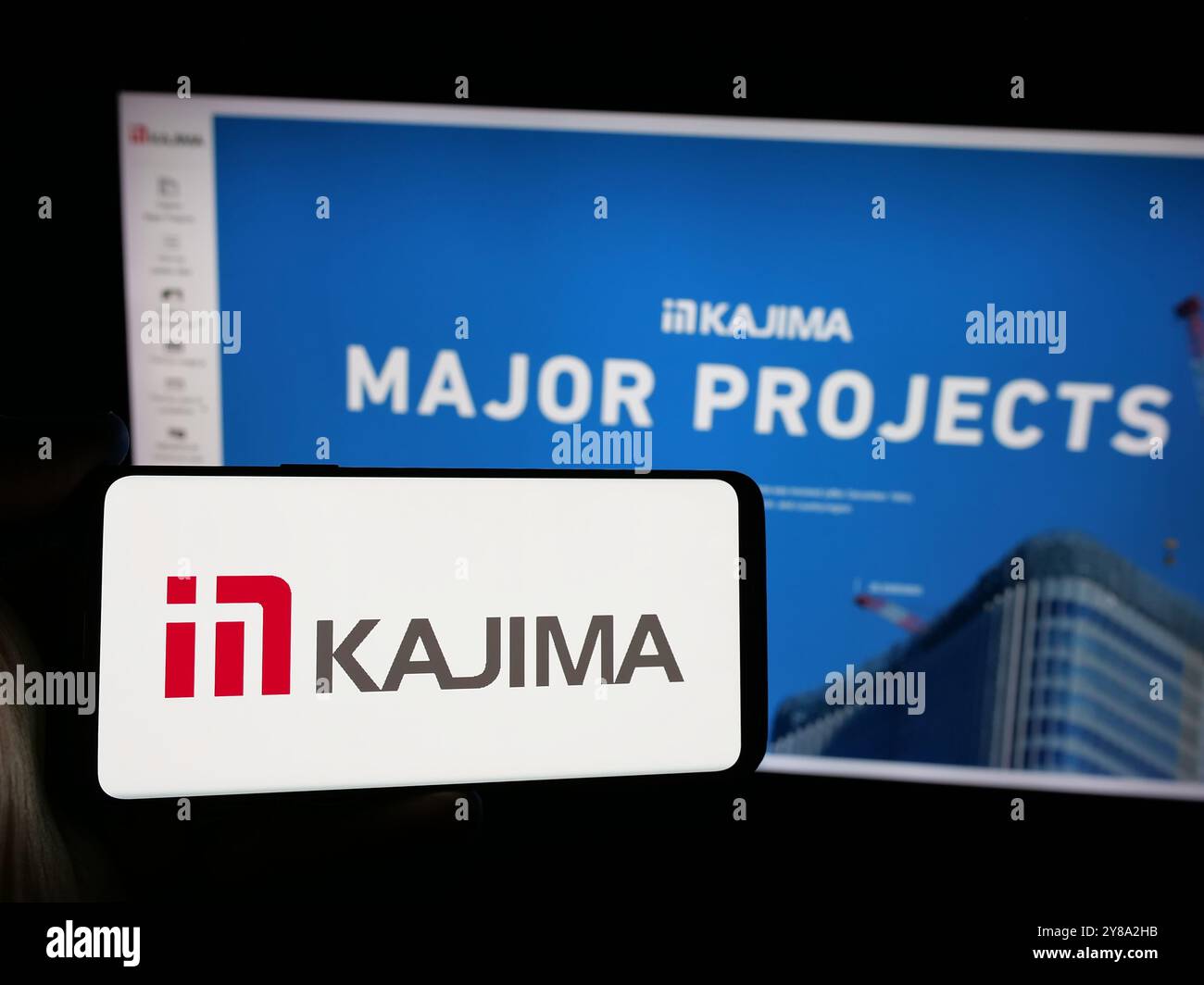 Person holding smartphone with logo of Japanese construction company Kajima Corporation on screen in front of website. Focus on phone display. Stock Photo