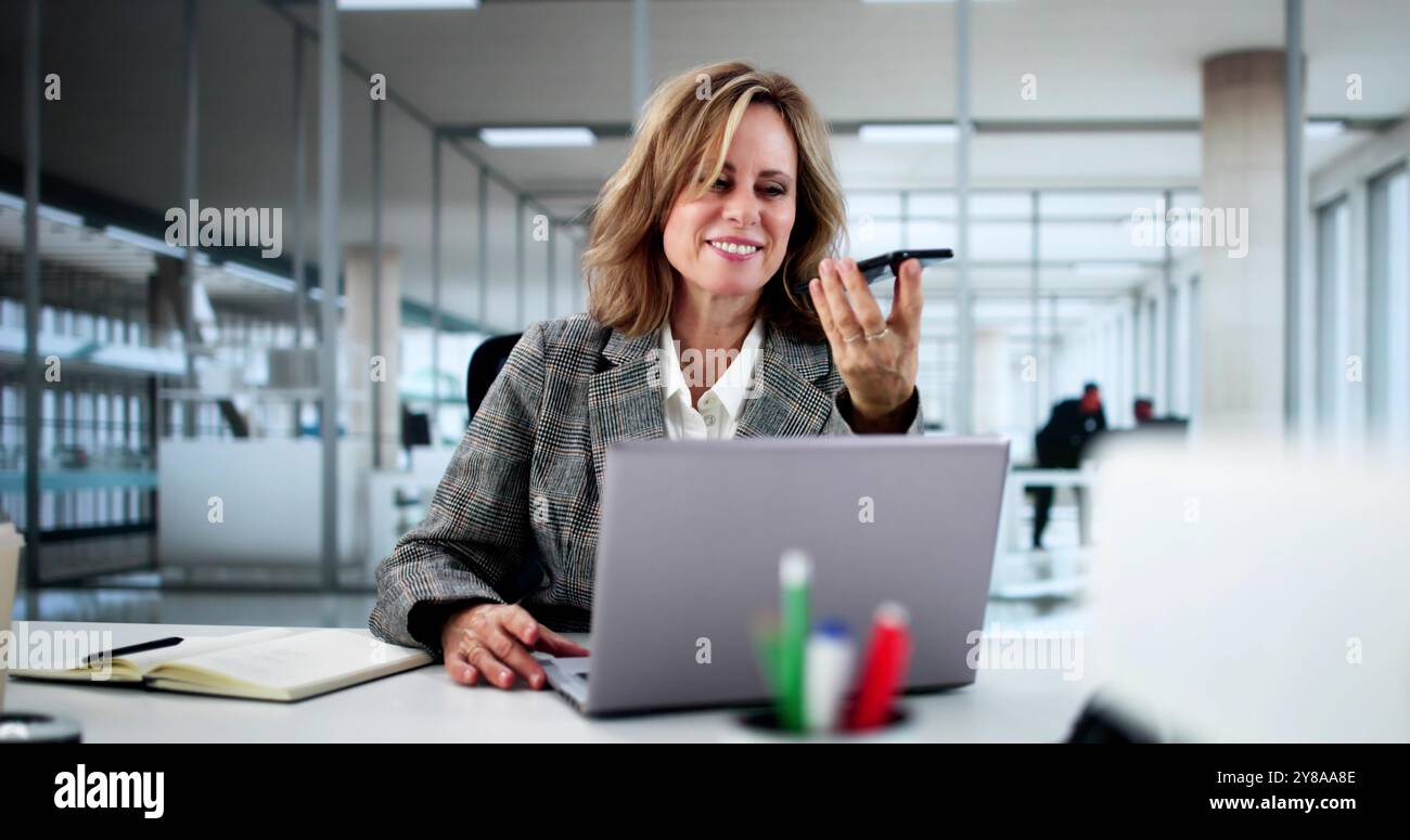 Professional Businesswoman Using Smartphone App For Client Call In Modern Office Setting With Laptop And Smiling Stock Photo
