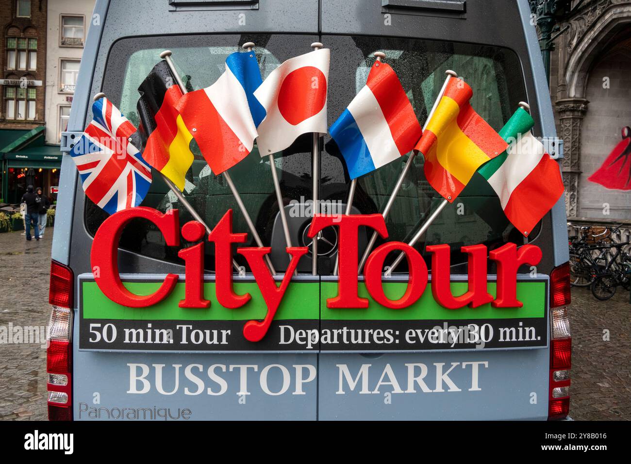 Belgium, Flanders, Bruges, Market Square, Grote Markt, flags on rear of City Tour bus in wet weather Stock Photo