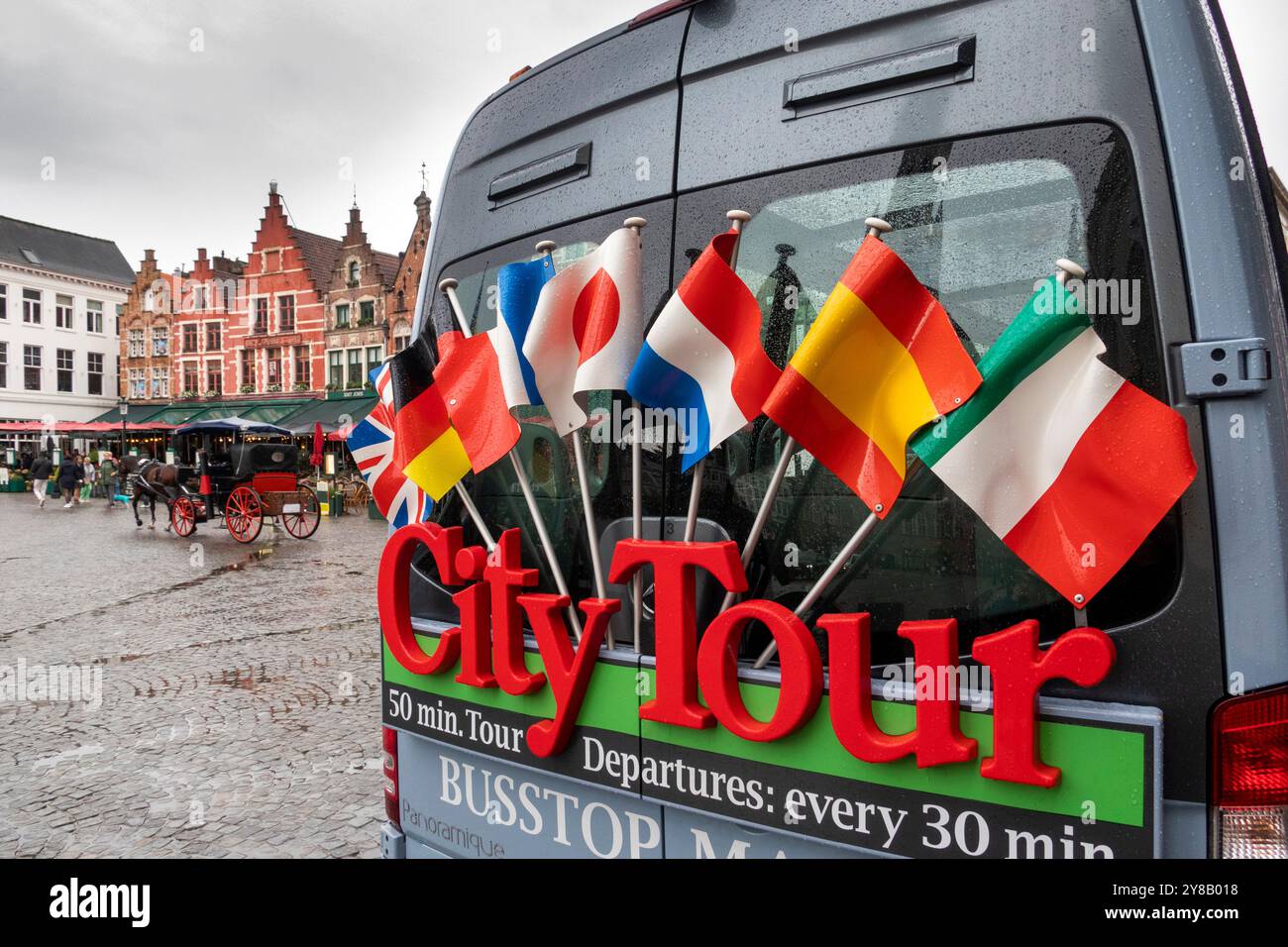 Belgium, Flanders, Bruges, Market Square, Grote Markt, flags on rear of City Tour bus in wet weather Stock Photo