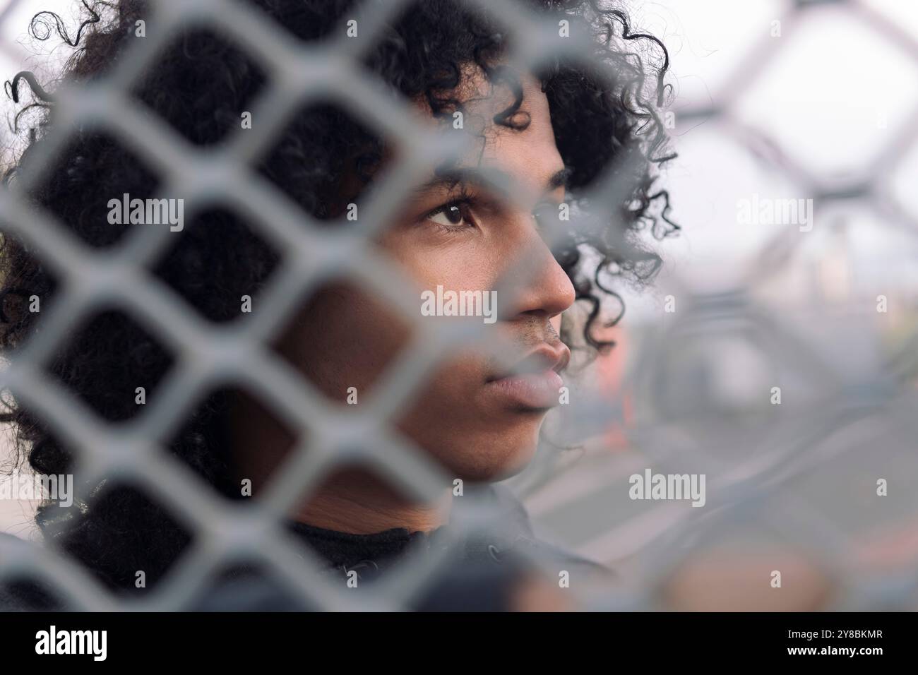 teen with curly hair behind metal chain link fence Stock Photo