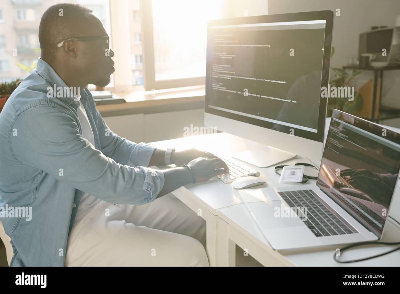 Side view shot of African American developer sitting at table and coding Stock Photo