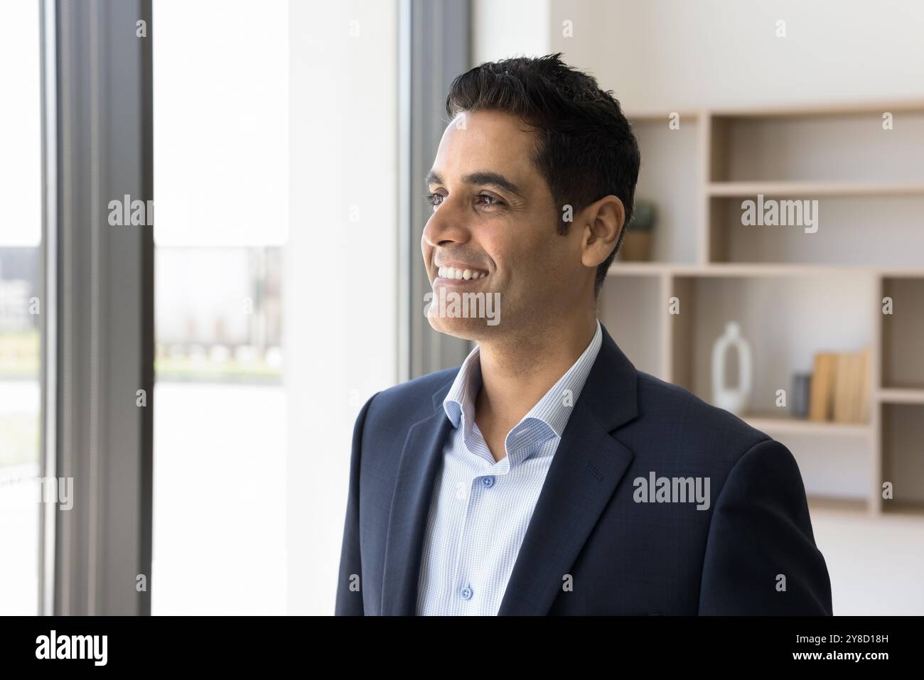 Happy young Indian man in formal suit look at window Stock Photo