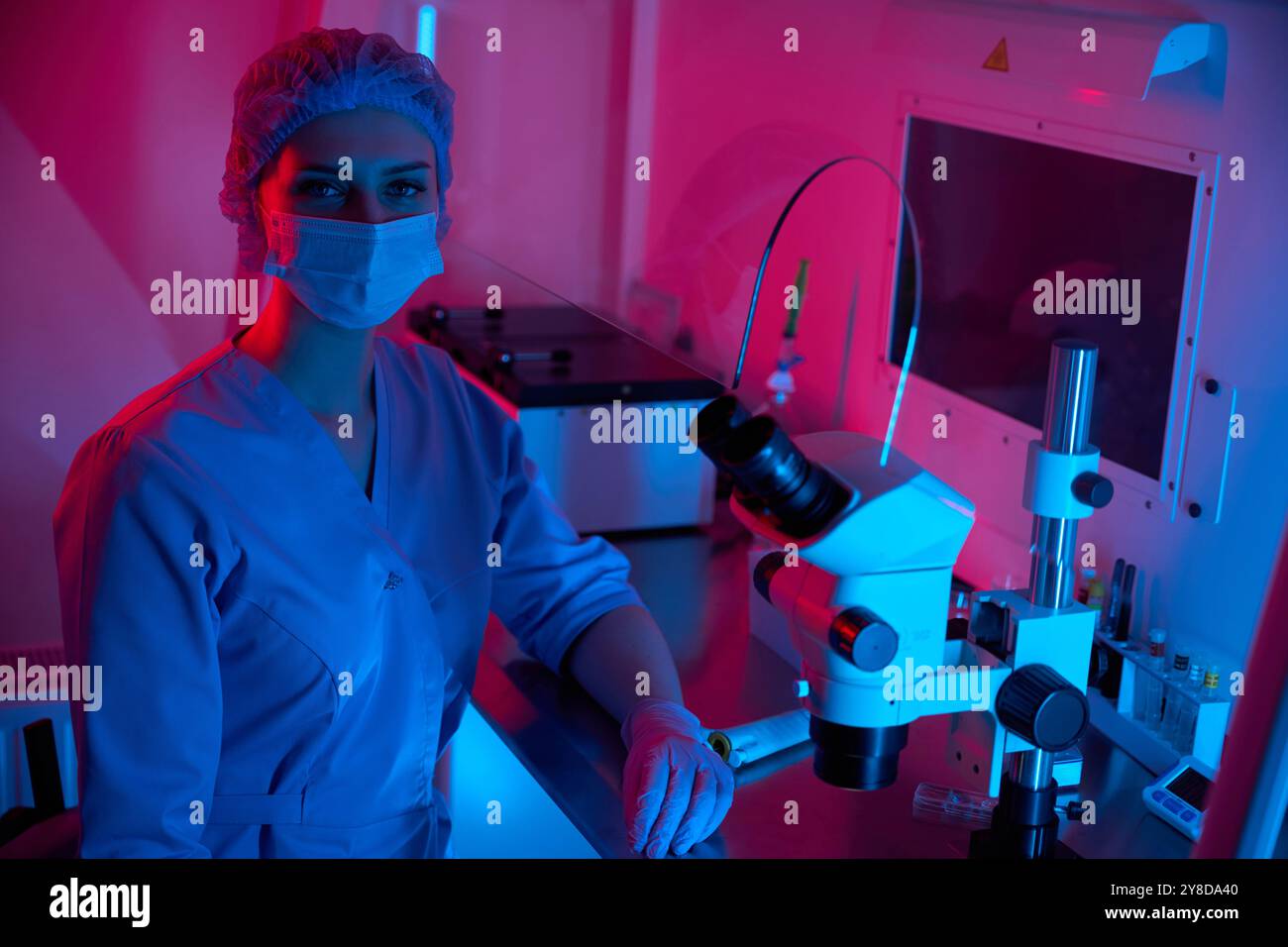 Scientist standing by a microscope in a brightly lit lab Stock Photo