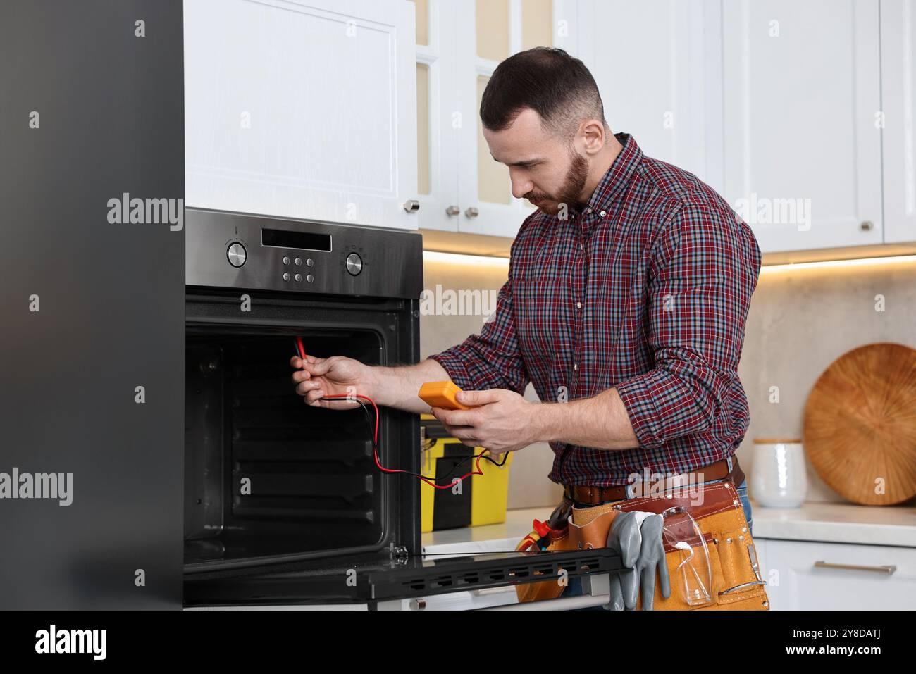 Repairman testing oven element with multimeter in kitchen Stock Photo