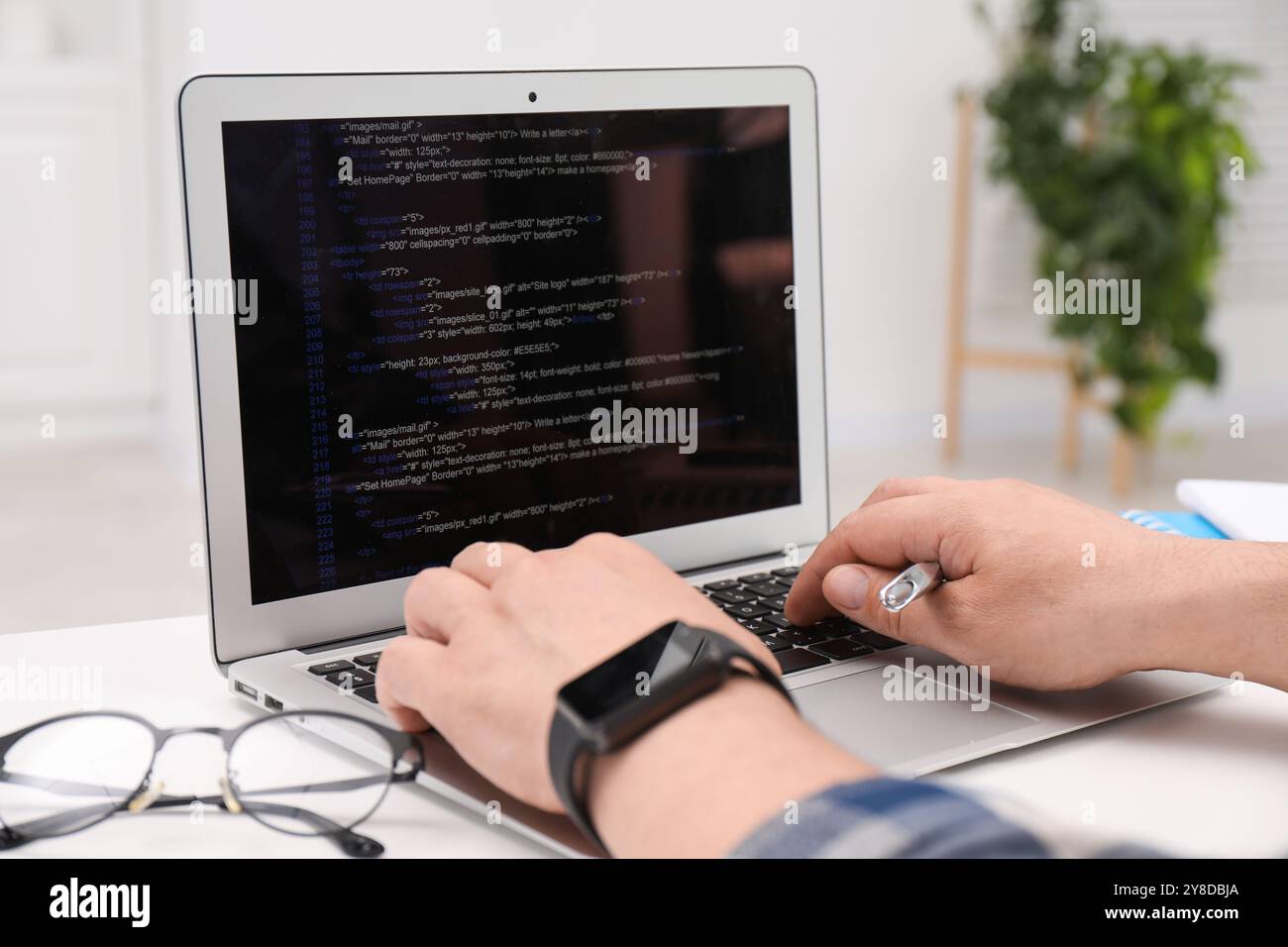 Programmer working with laptop at white desk in office, closeup Stock Photo