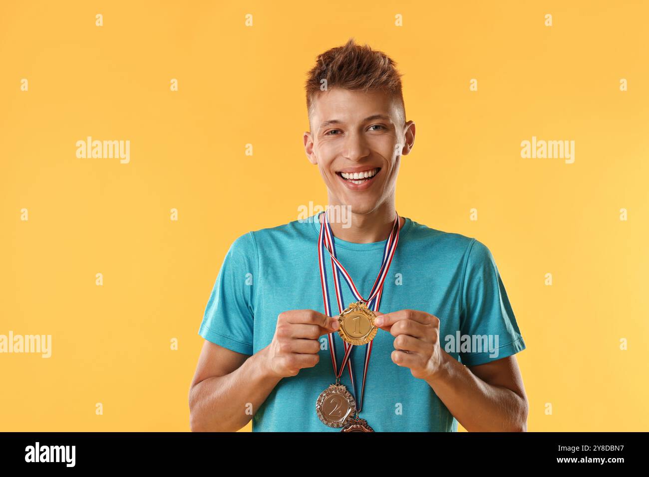 Happy winner with different medals on yellow background Stock Photo - Alamy