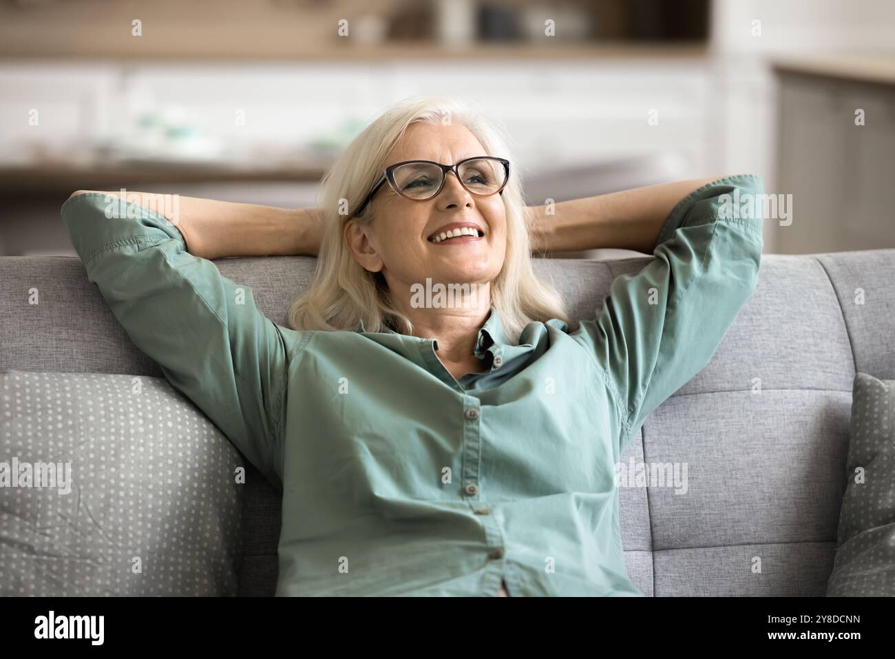 Satisfied older woman resting leaned on soft couch Stock Photo