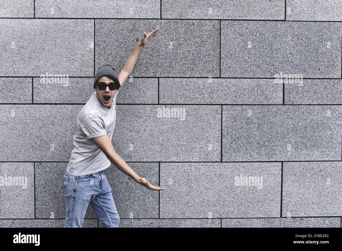 Cheerful guy dressed in gray t-shirt, sunglasses and hat at the street, show a big sale, or nice offer. Advertise concept. People, travel and tourism Stock Photo