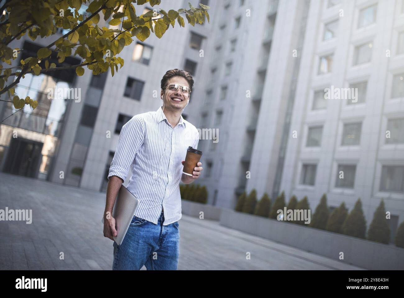 Cheerful young handsome well dressed man holding laptop computer and cup of coffee Stock Photo