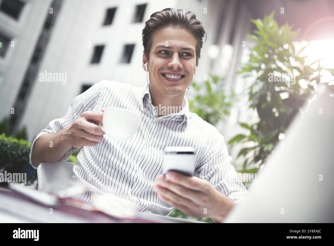 Happy handsome businessman looking at computer screen while typing something on laptop keyboard during work break outdoors, businessman with headphone Stock Photo