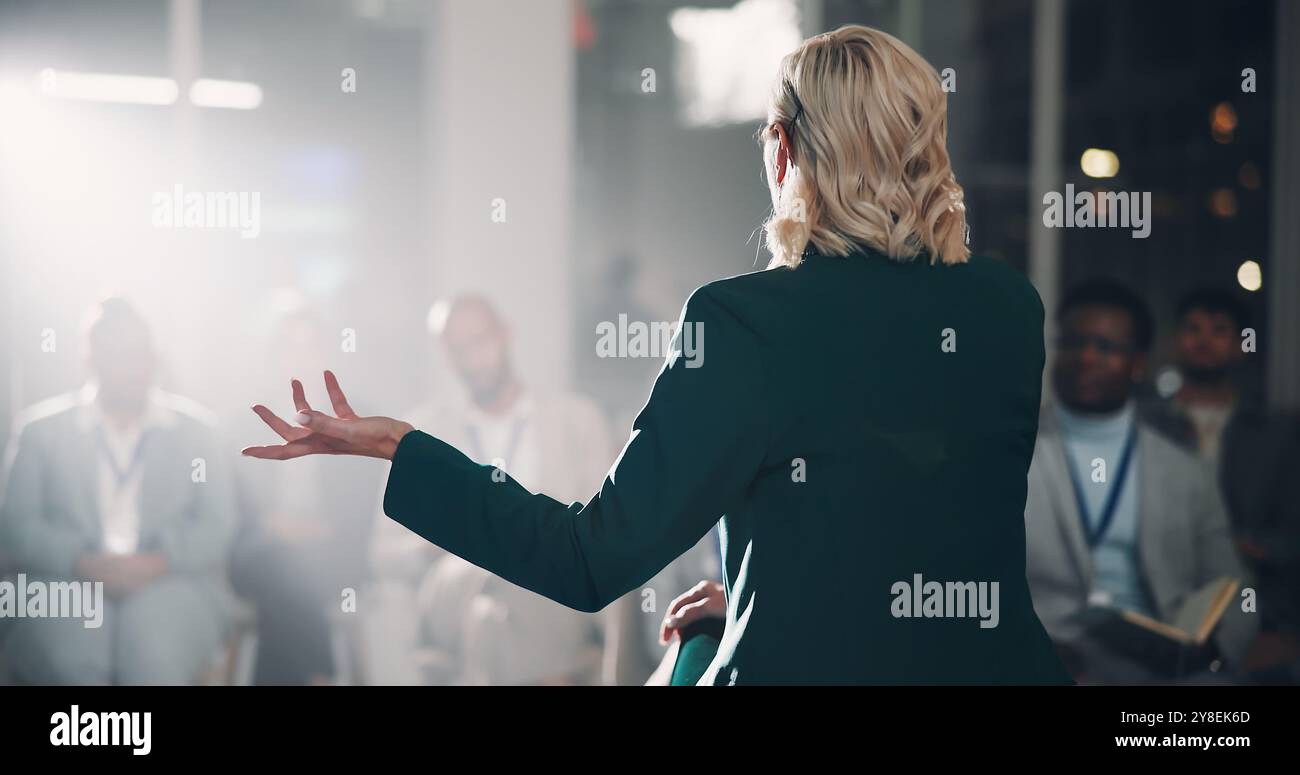 Back, woman and speaker with presentation for crowd speech, workshop and coaching conference on stage. Professional, presenter and mic for Stock Photo