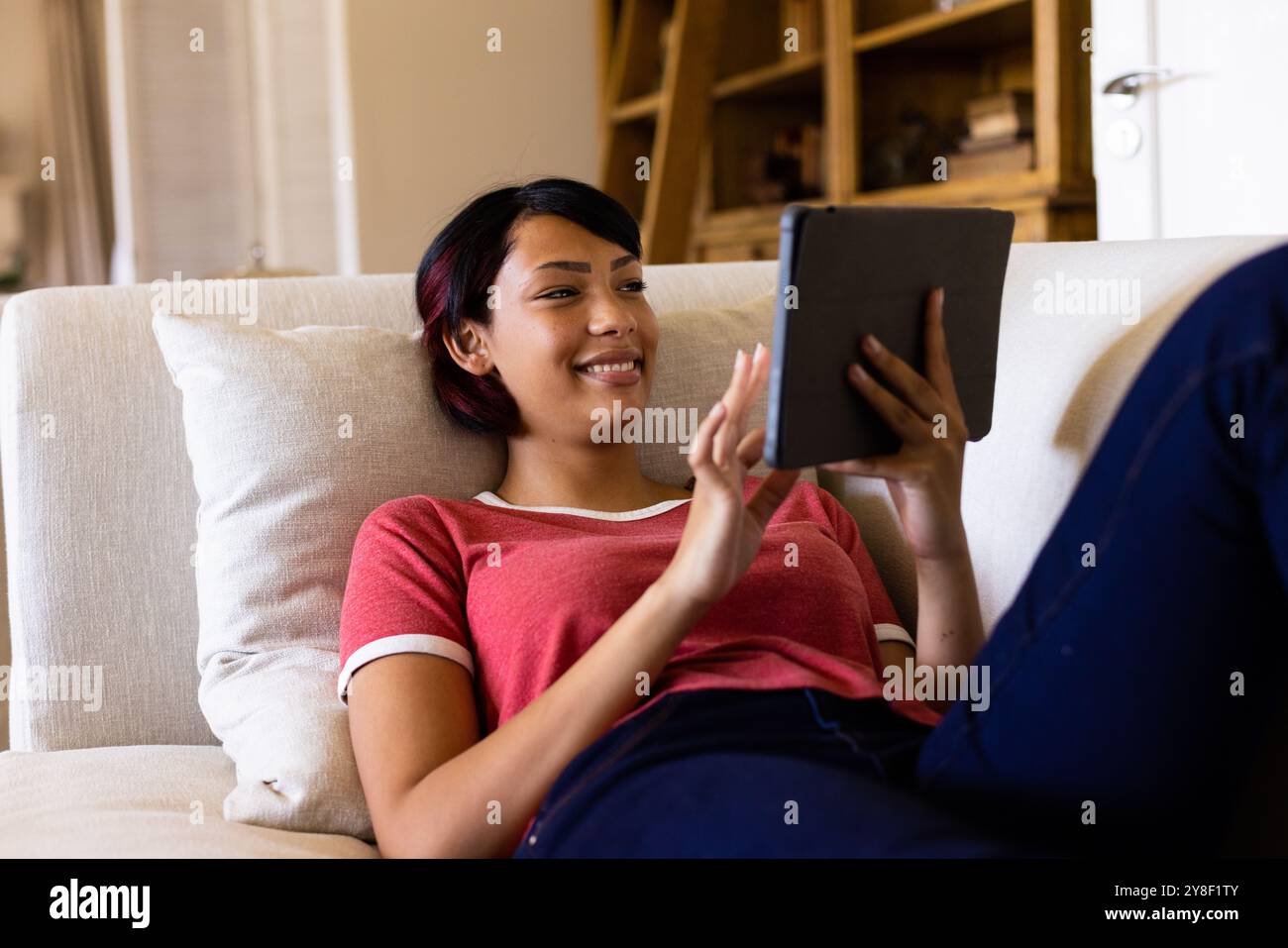 Happy biracial woman lying on couch and using tablet Stock Photo - Alamy