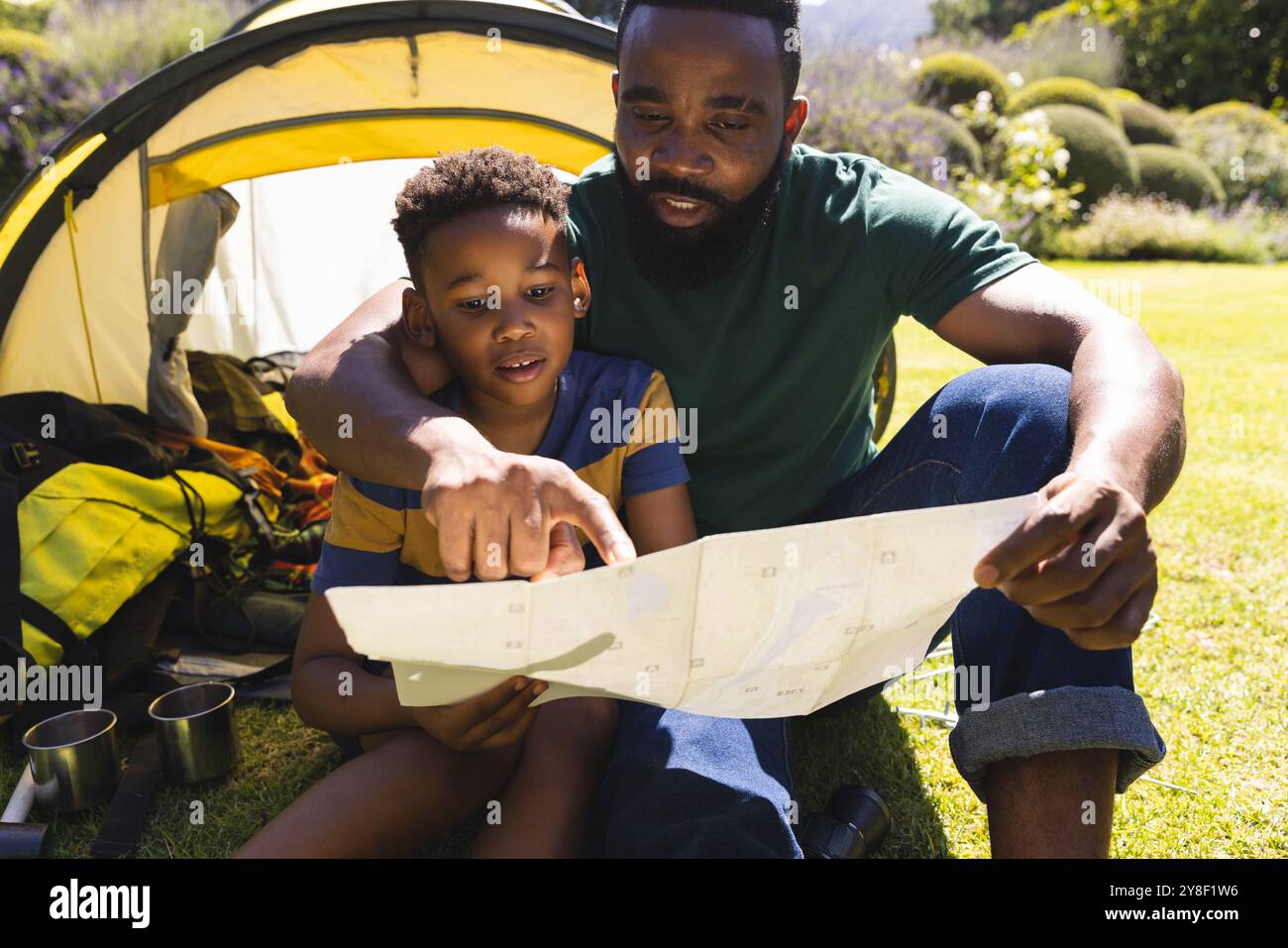 happy-african-american-father-and-son-sitting-on-grass-and-reading-map