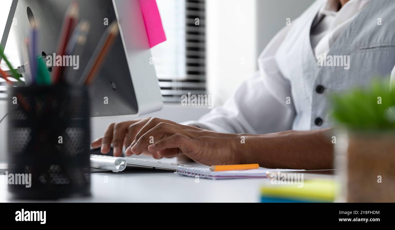 Side view mid section of a young African American man sitting at a desk ...