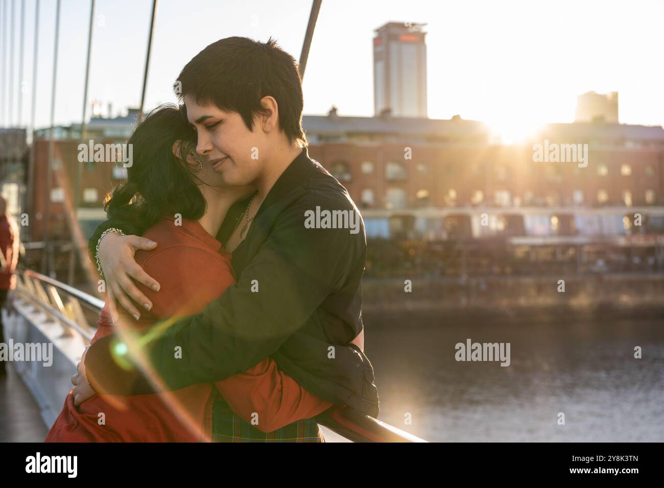 Young LGBT couple of women embracing each other on a bridge, creating a ...