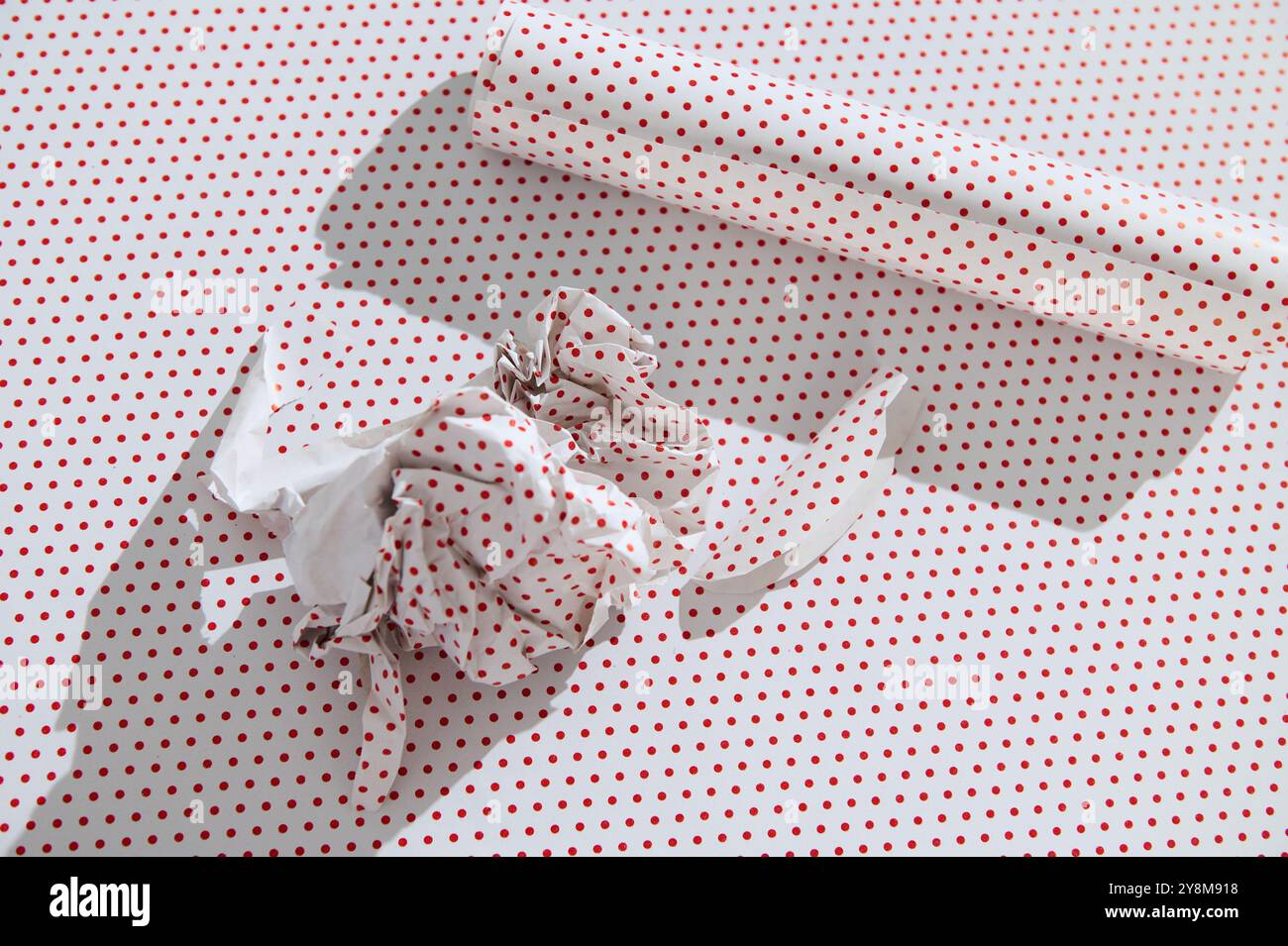 Crumpled red polka dot wrapping paper with a roll on a matching background, highlighting holiday or creative concepts. Stock Photo