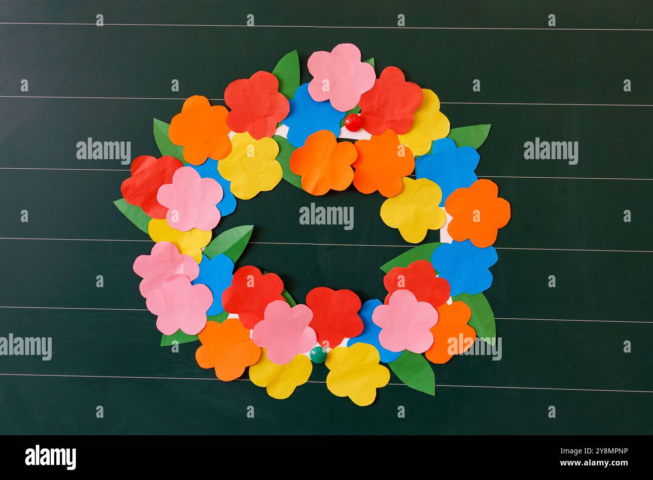 A bright wreath of paper flowers with a sun on a green board is a ...