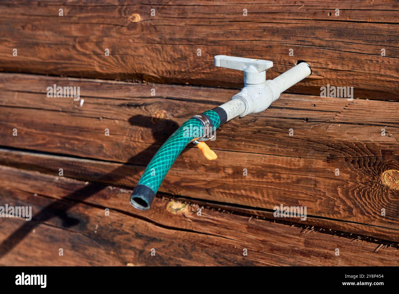 A close-up view of a green garden hose nozzle on a rustic wooden surface, bathed in natural sunlight Stock Photo