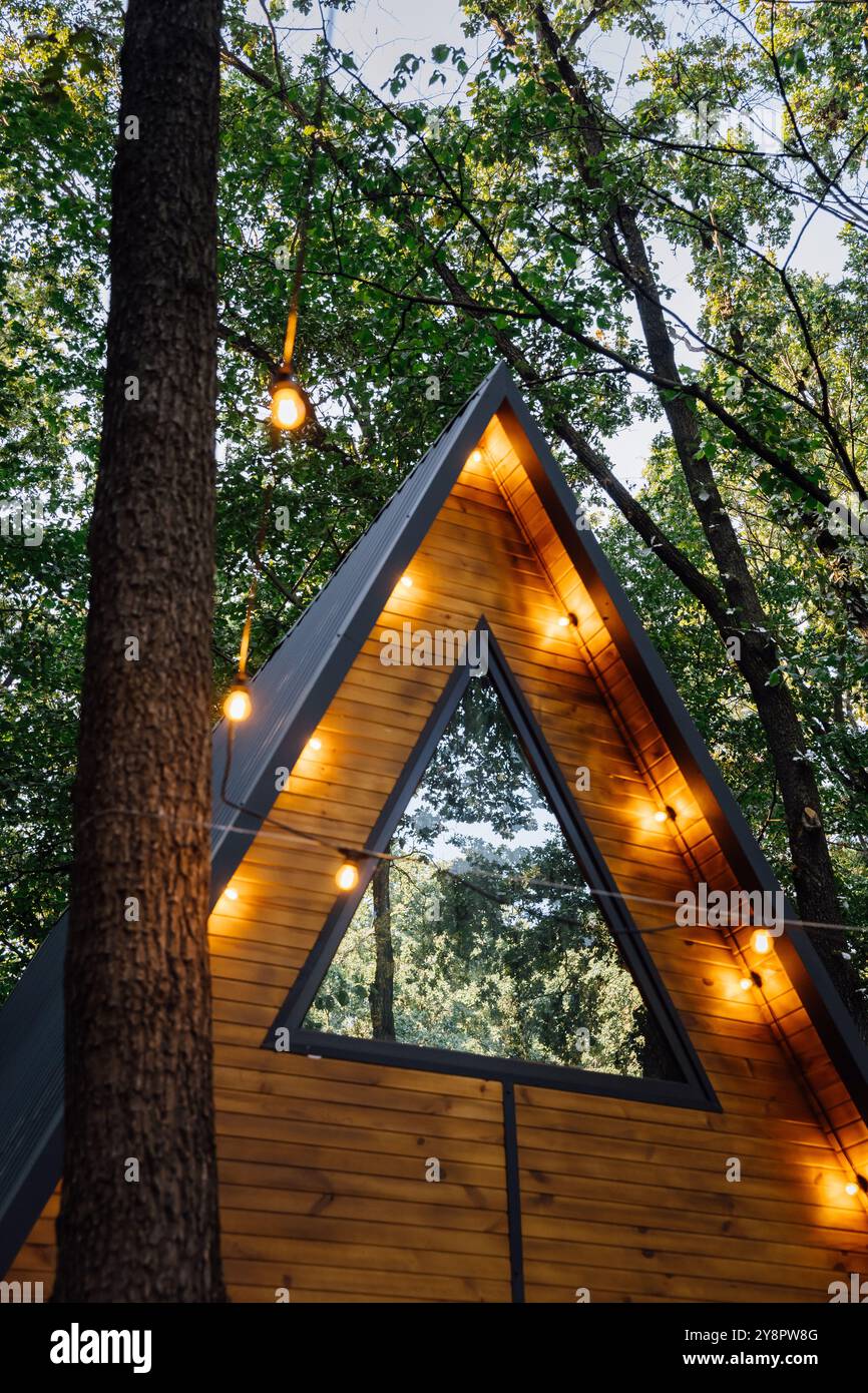 Modern A-frame wooden cabin with warm glowing lights, surrounded by ...