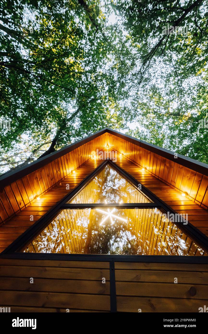 Modern A-frame wooden cabin with warm glowing lights, surrounded by ...