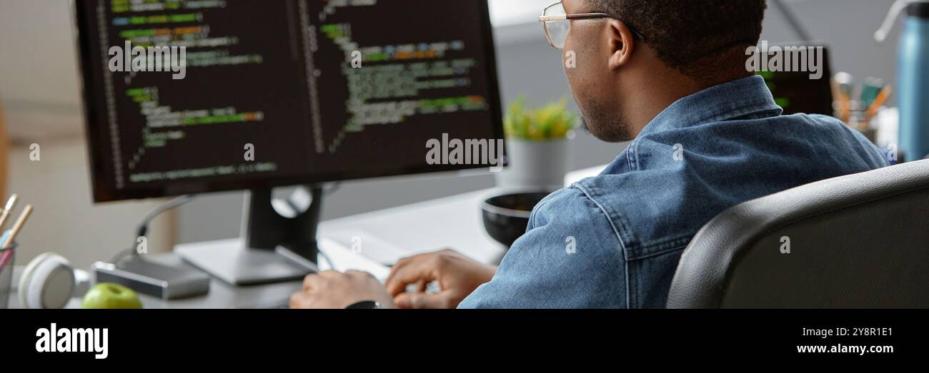 Website header shot of African American male IT developer code programming on computer while sitting at desk in office, copy space Stock Photo