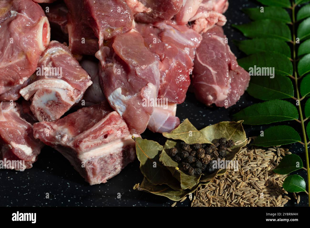 Freshly cut goat meat pieces with herbs and spices like bay leaves, cumin seeds, and peppercorns. Perfect for food preparation, recipes, and culinary Stock Photo