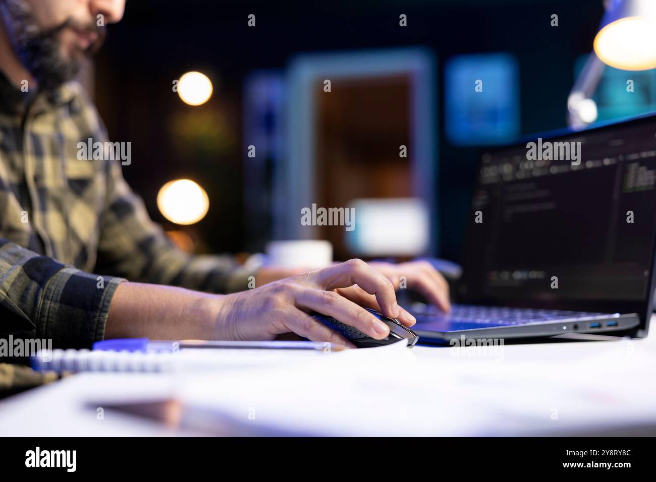 Closeup of male individual typing on a laptop and using a mouse to manage software codes and systems. Bearded man monitoring database network on his portable computer. Stock Photo