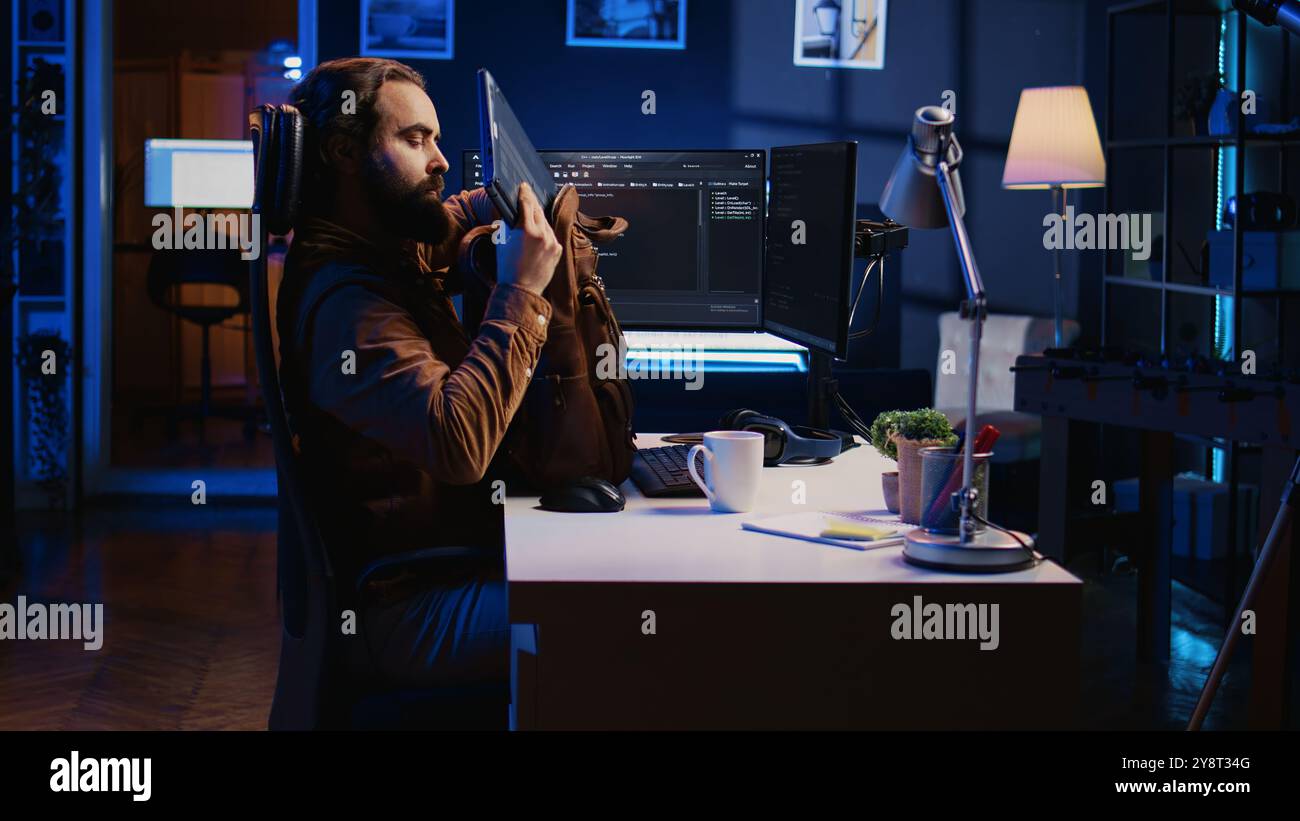 Software designer finishing remote job shift, packing backpack, leaving office after finishing coding project. IT professional putting laptop in bag, sitting up from desk chair, camera B Stock Photo