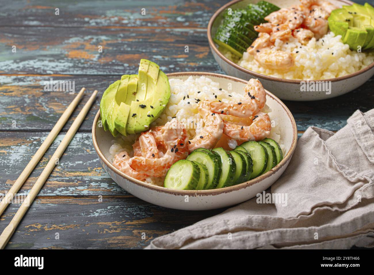 White ceramic bowl with rice, shrimps, avocado, vegetables and sesame seeds and chopsticks on colourful rustic wooden background front view. Healthy a Stock Photo