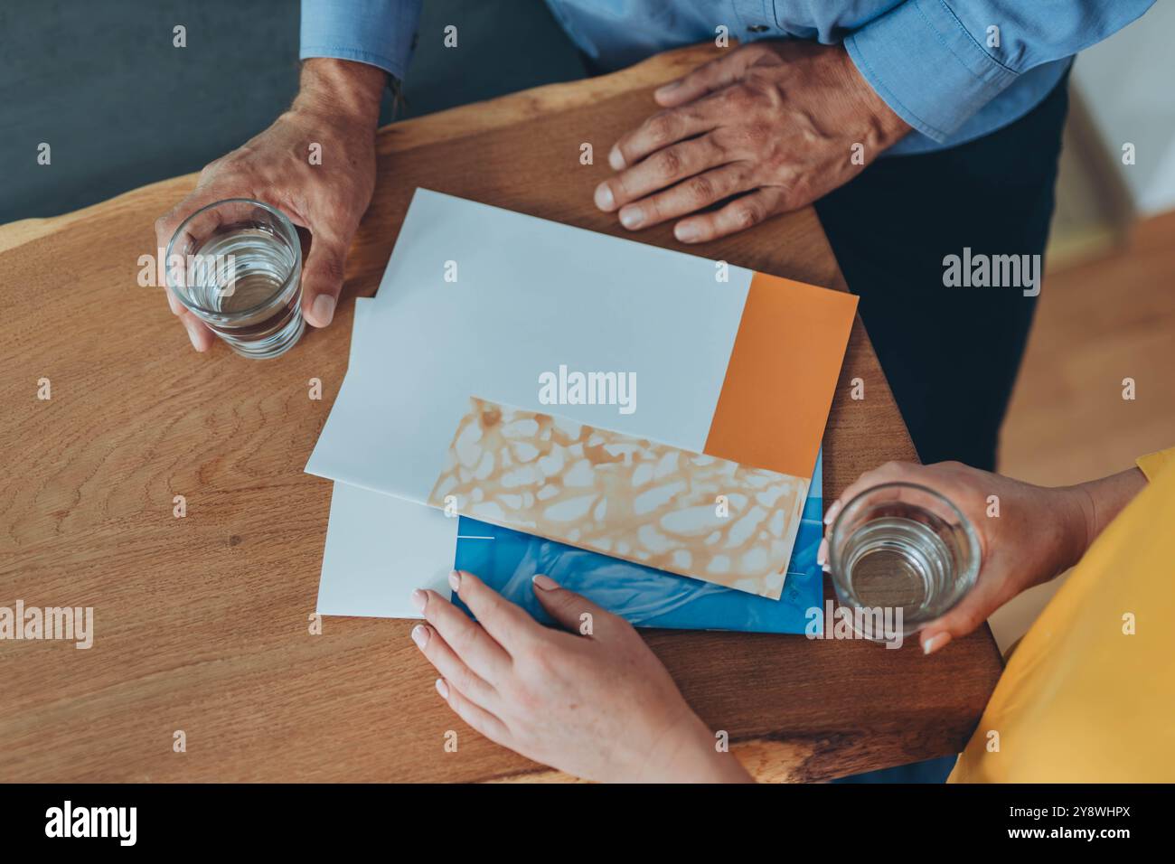 Two people holding glasses of water, reviewing documents on a wooden table, discussing details. High quality photo Stock Photo