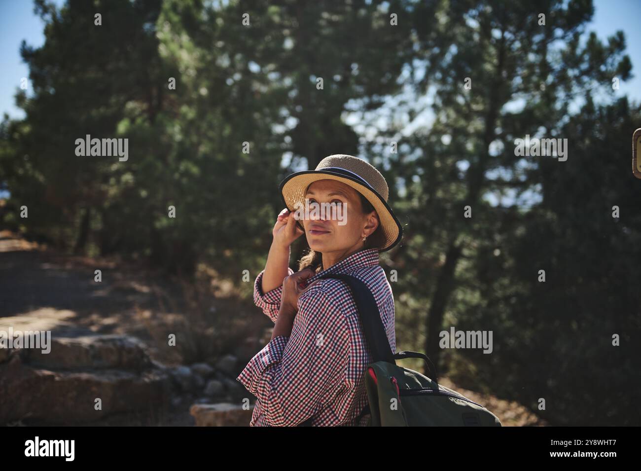 Woman exploring a peaceful forest trail, wearing a hat and backpack ...