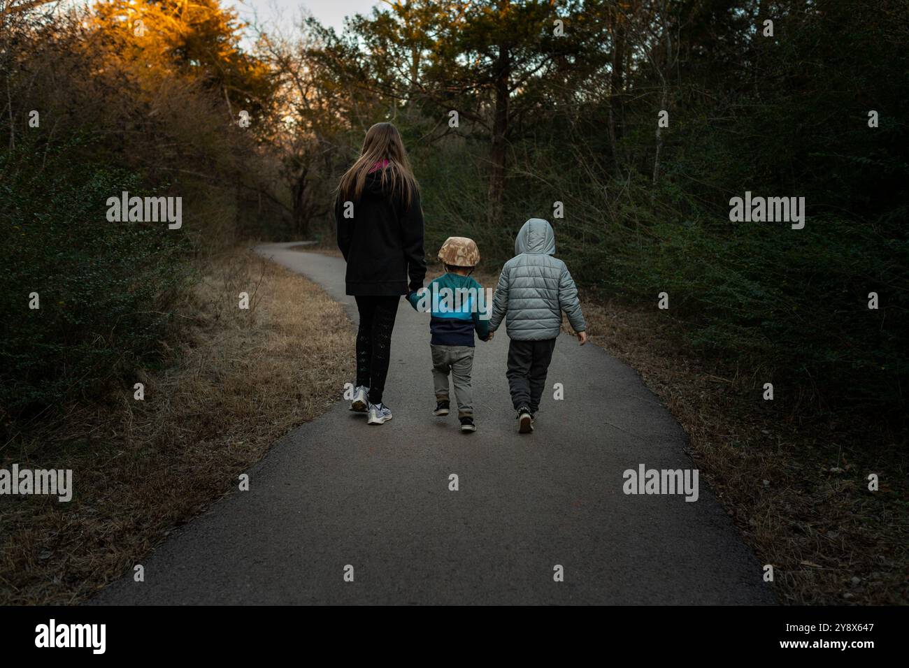 Three siblings hold hands while walking a path surrounded by nature ...