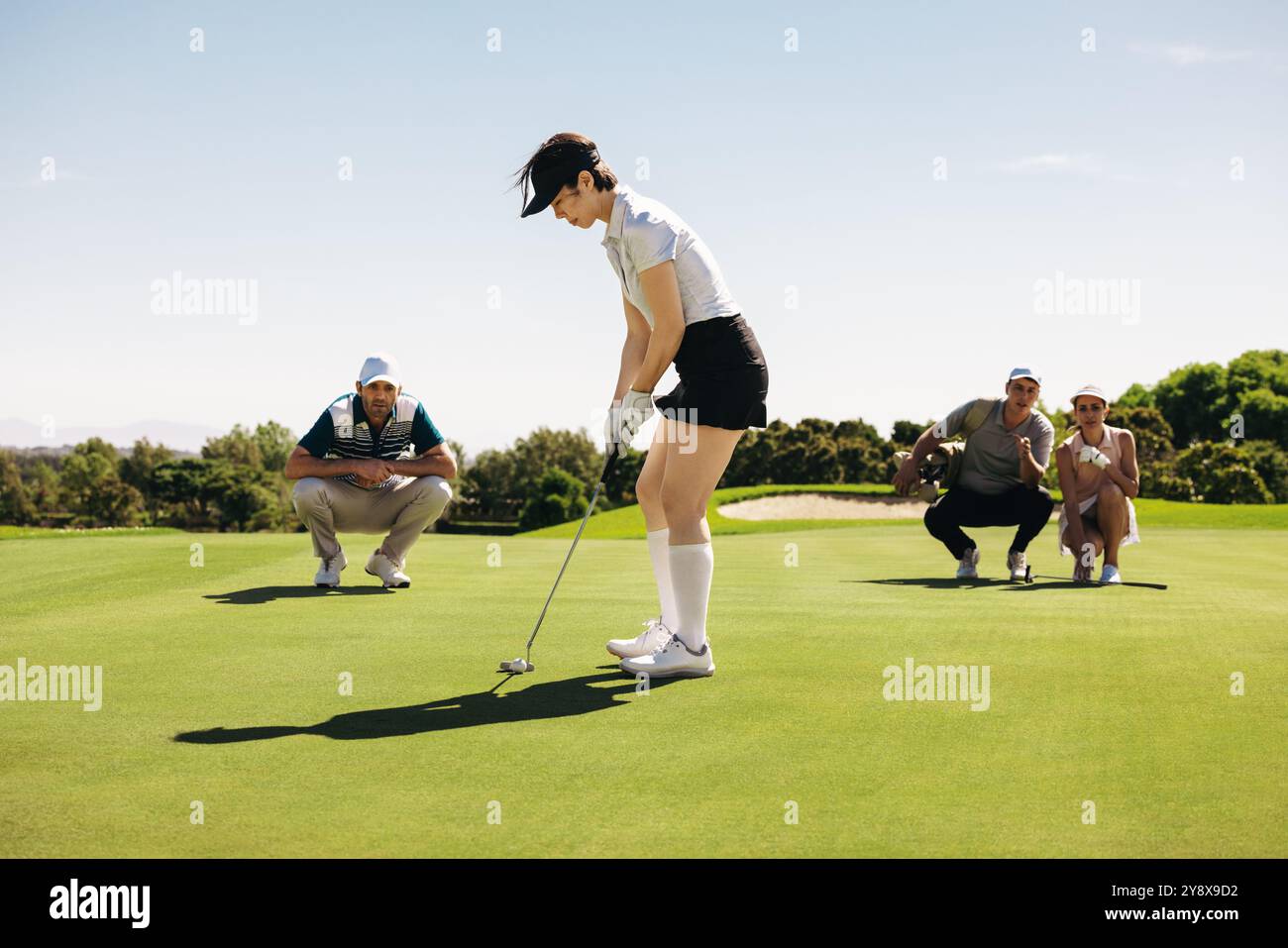 A woman in putting stance aims on the green, surrounded by fellow ...