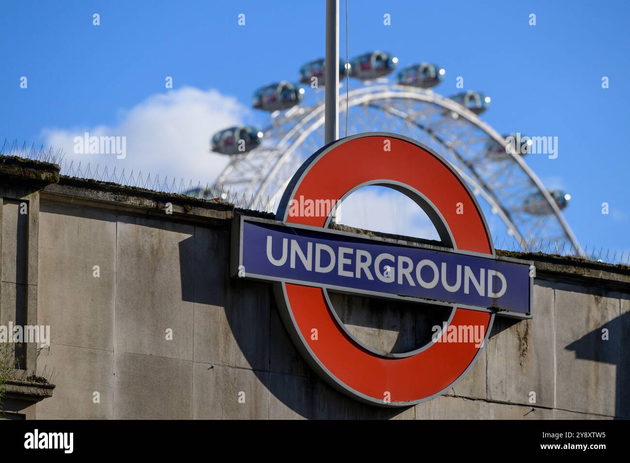 The roundel of Embankment Underground Station with the London Eye in the background. Embankment Underground Station, London, UK.  28 Sep 2024 Stock Photo