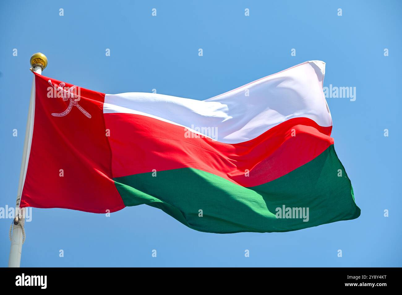 Flag of Oman on flagpole waving against blue sky Stock Photo