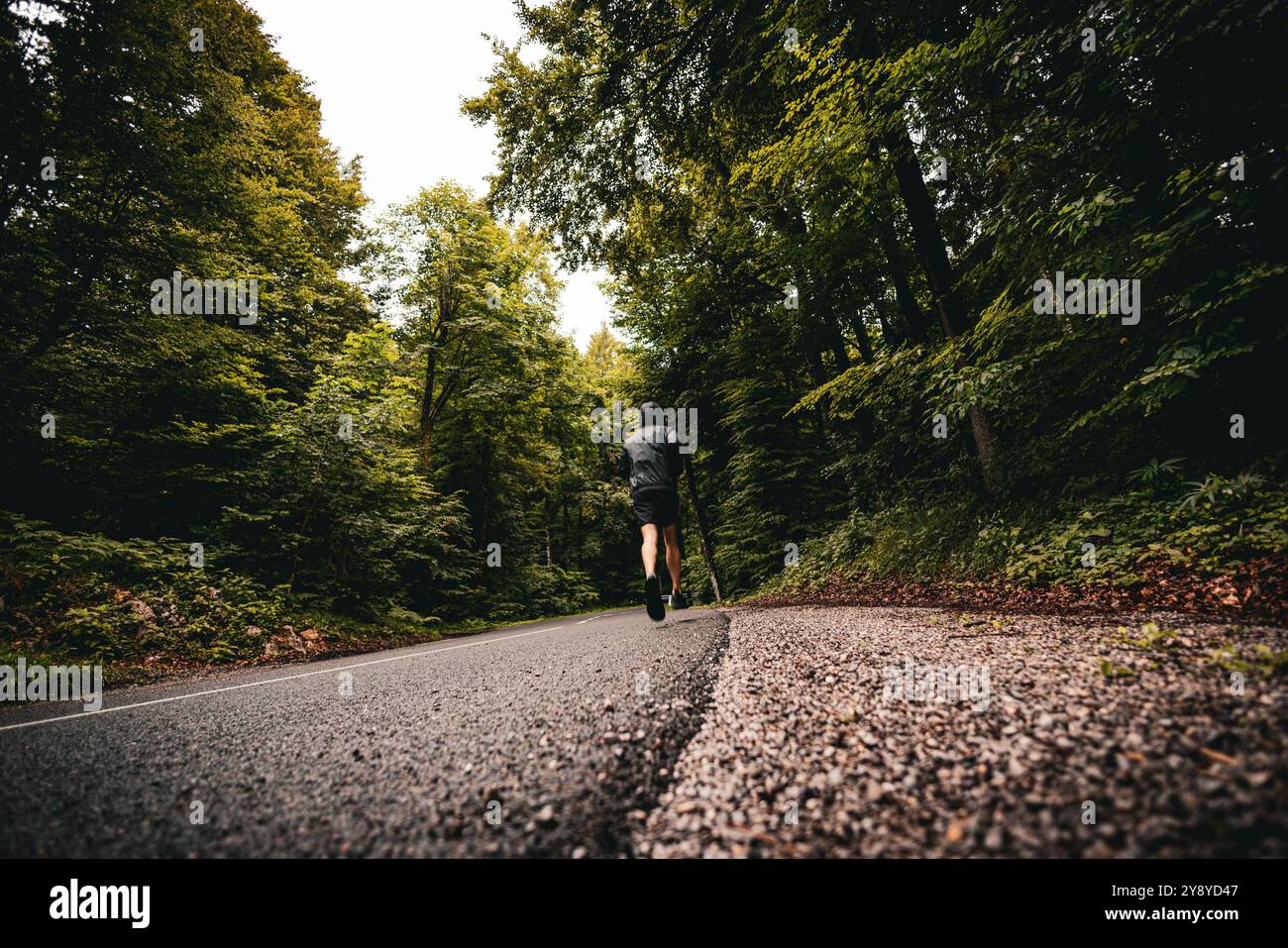 Unrecognized athletic build man running on an asphalt road. From behind ...