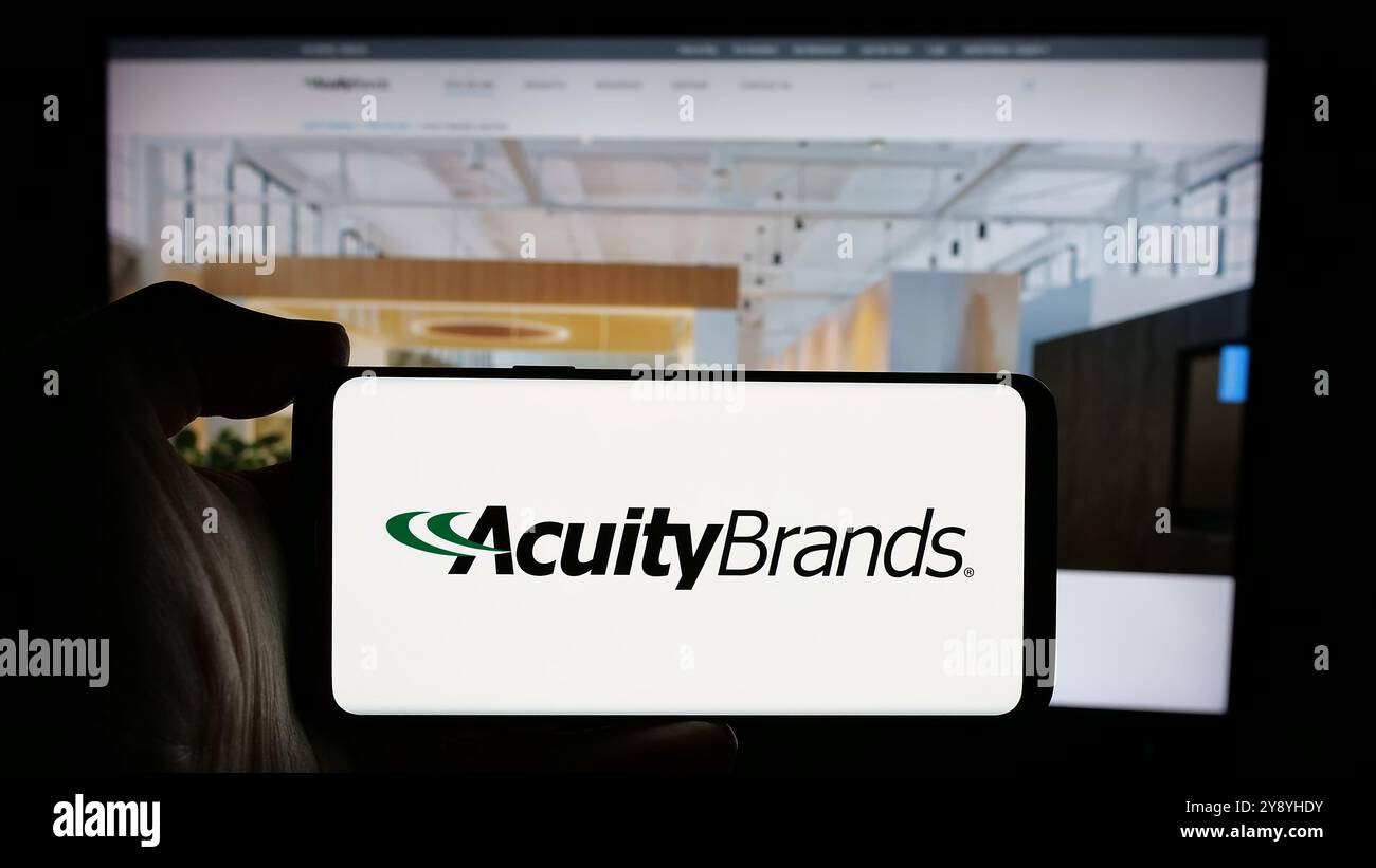 Person holding cellphone with logo of US lighting company Acuity Brands Inc. on screen in front of business webpage. Focus on phone display. Stock Photo