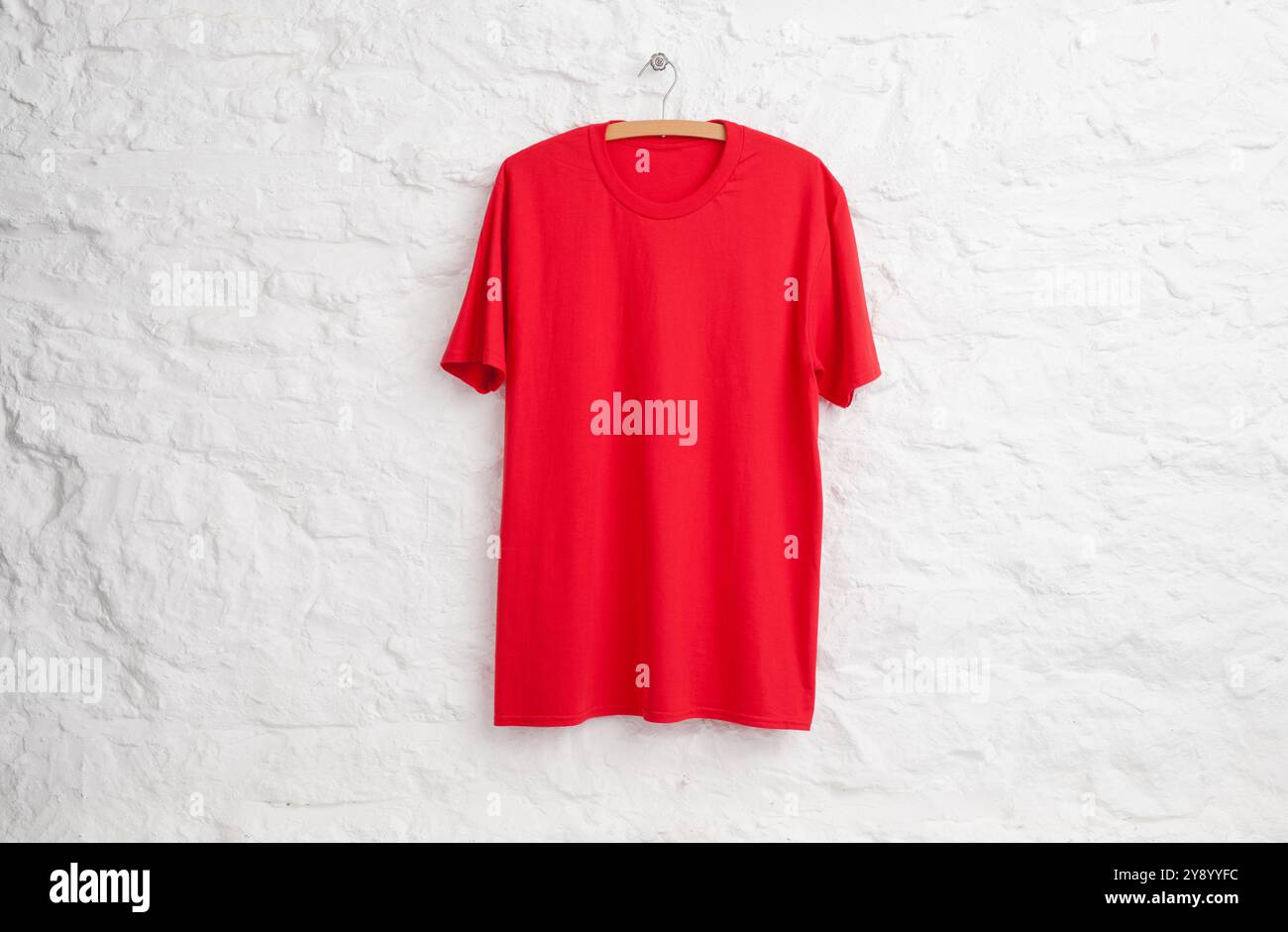 Red teeshirt hanging in front of white painted stone wall Stock Photo