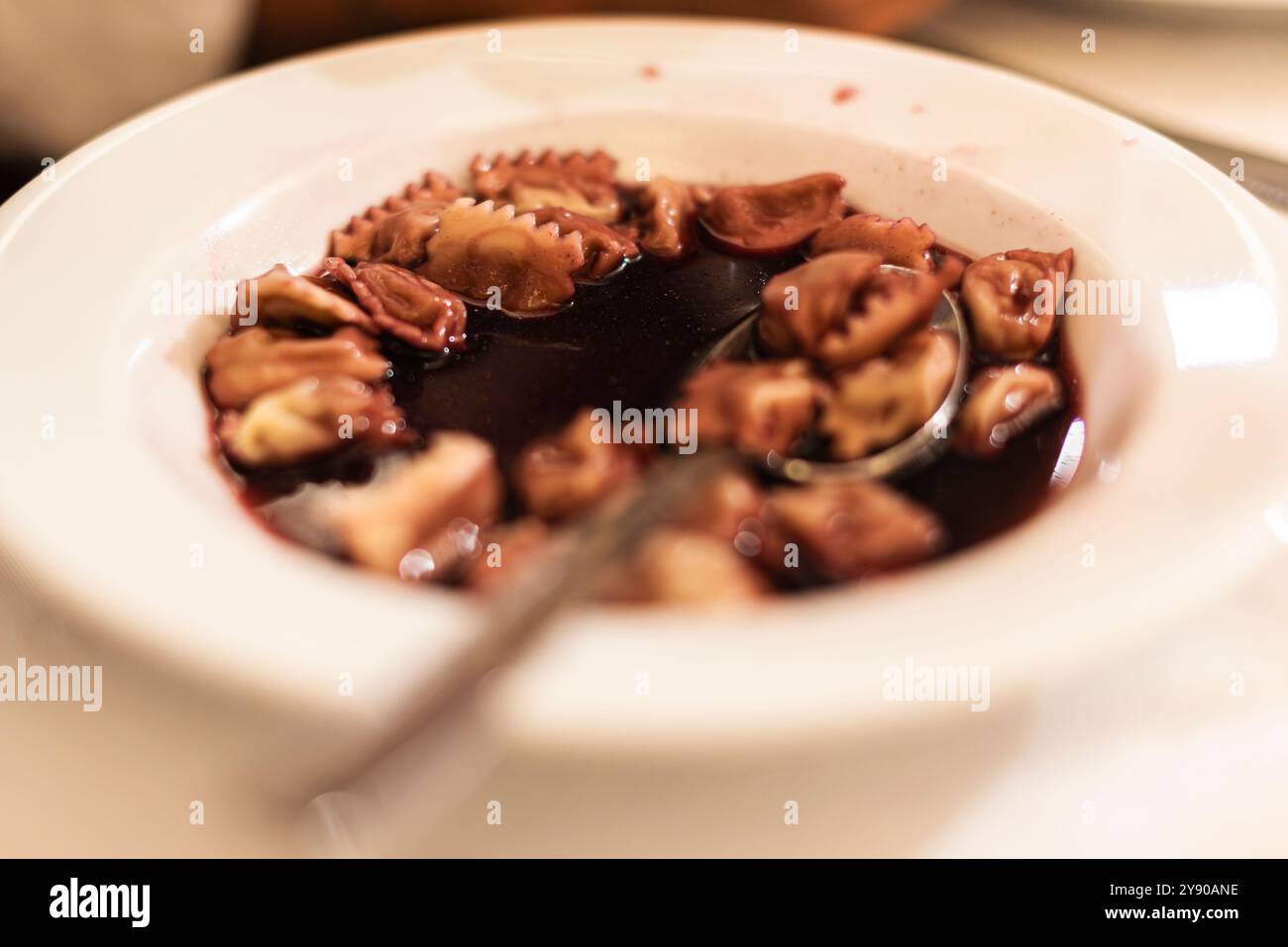 Once upon a time the monks used to confort the pilgrims in the cold winter, serving Ravioli in a plate of warm red wine. Ravioli nel vino. Stock Photo