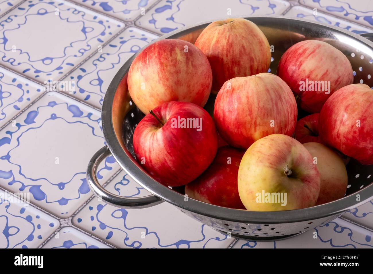 Red apples lie in a metal colander on a table with a blue and white ...