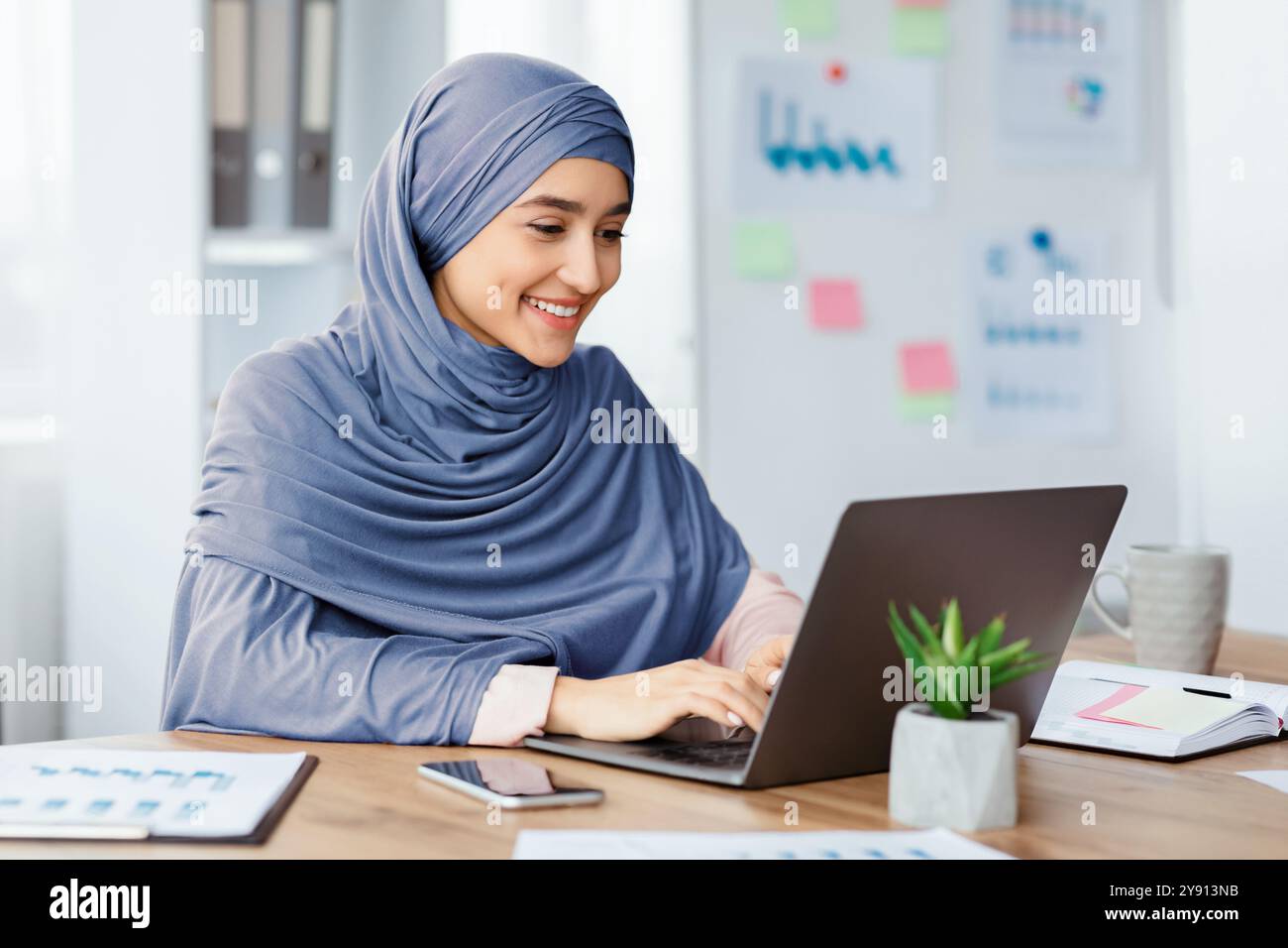 Happy islamic woman in hijab working on laptop in office Stock Photo ...