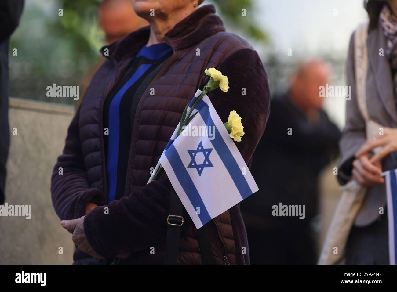 Details with the hands of a woman holding the Israeli flag and a flower during a ceremony commemorating the October 2023 attacks. Stock Photo