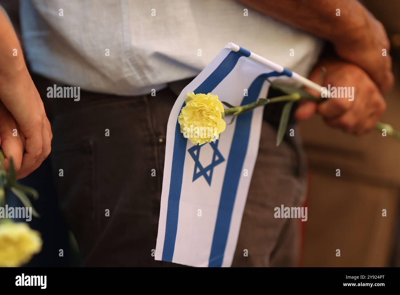 Details with the hands of a man holding the Israeli flag and a flower during a ceremony commemorating the October 2023 attacks. Stock Photo