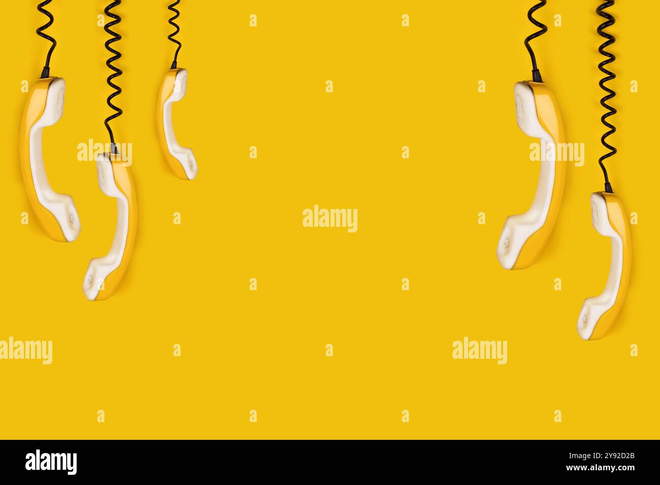 A few yellow old phone handsets dangle on wire. yellow background banner copy space Stock Photo