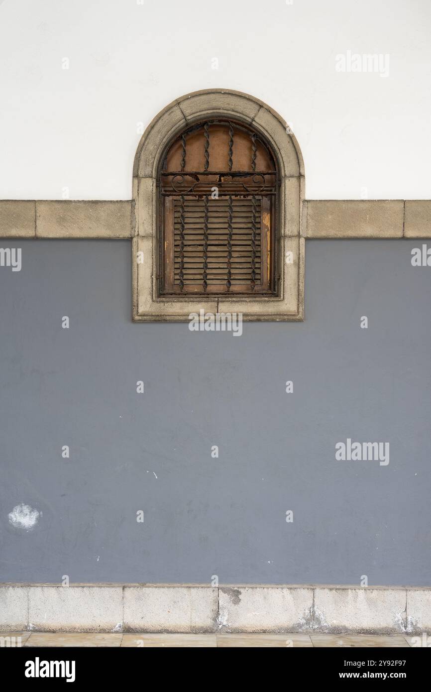 Arched window with wooden shutter on two-toned wall Stock Photo